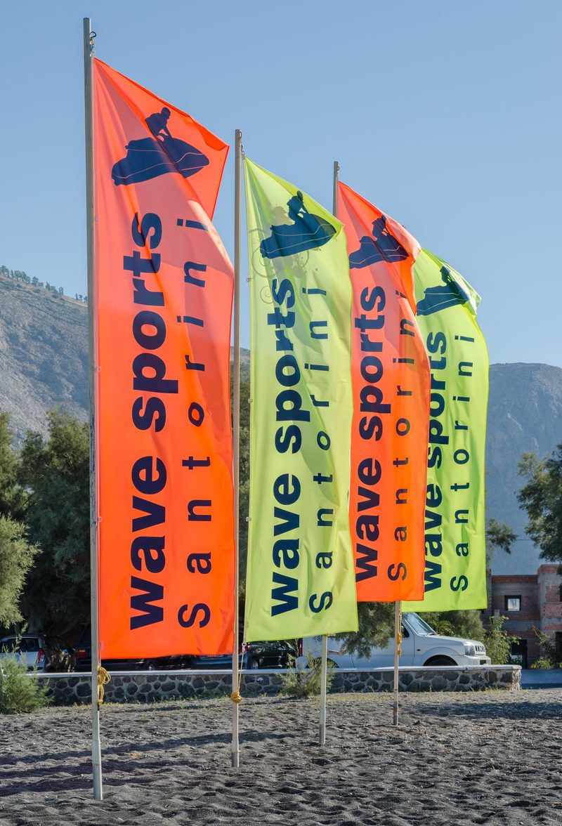 A serene view of Perissa Beach in Santorini, Greece, with black sand and clear blue waters.
