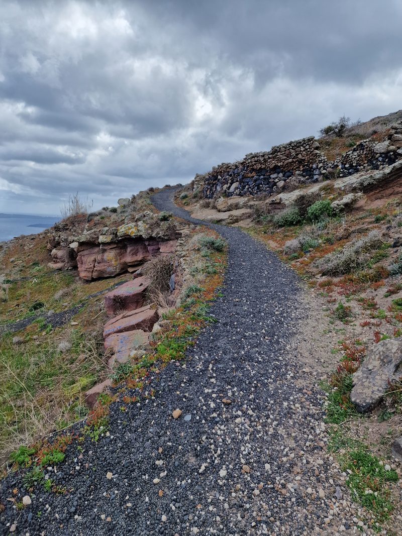 A narrow gravel walking track along the clifftop, hemmed in by low stone walls and volcanic rock