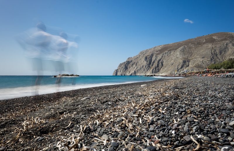 A long-exposure shot of a man walking along Kamari Beach in Santorini.