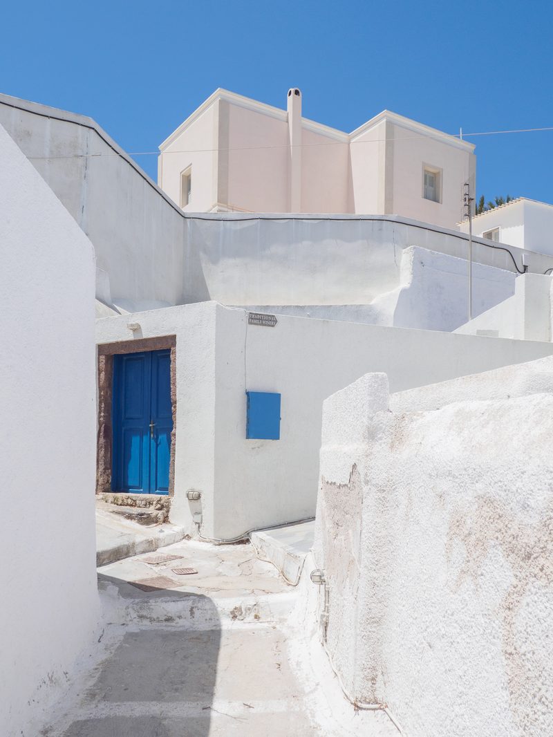 A narrow street in Megalochori, Santorini, lined with traditional whitewashed buildings.