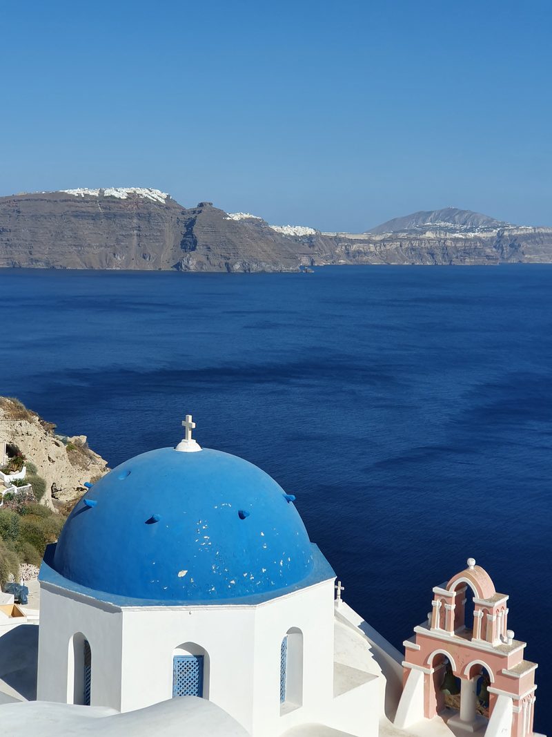 One of Oia's blue-domed churches, with the caldera cliffs stretching into the distance behind it