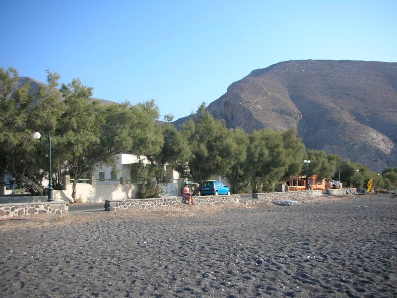 A sandy beach with sunbeds and umbrellas along the Perissa coast of Santorini.