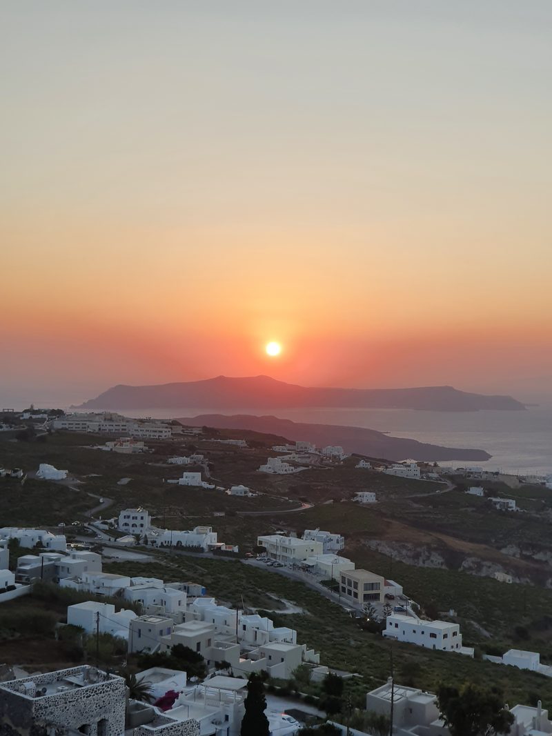 Sunset seen from the hillside near Pyrgos, the sun sinking over the sea beyond dark rock outcrops