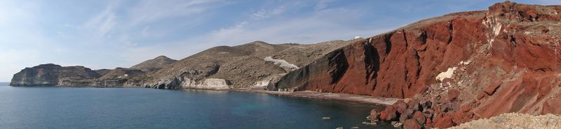 A vibrant red sand beach with dramatic cliffs at Red Beach, Santorini, Greece.