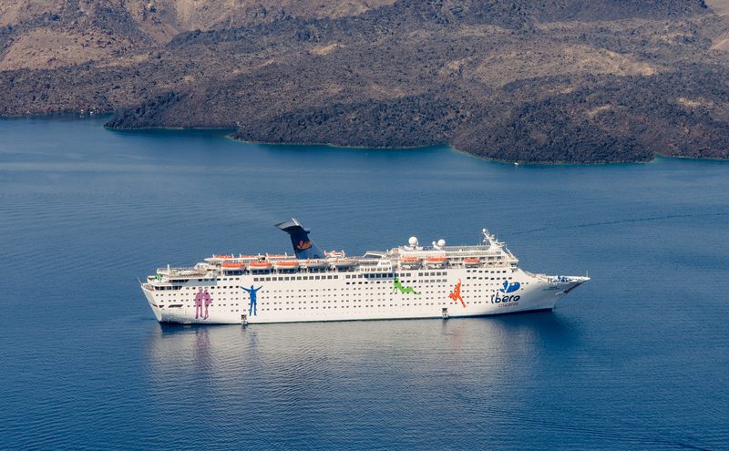 A cruise ship in Santorini's caldera with the volcanic island Nea Kameni in the background.