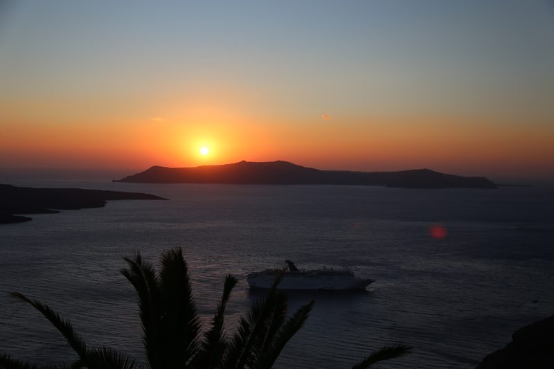 A serene sunset over the caldera in Santorini, Greece, with a boat cruising by.
