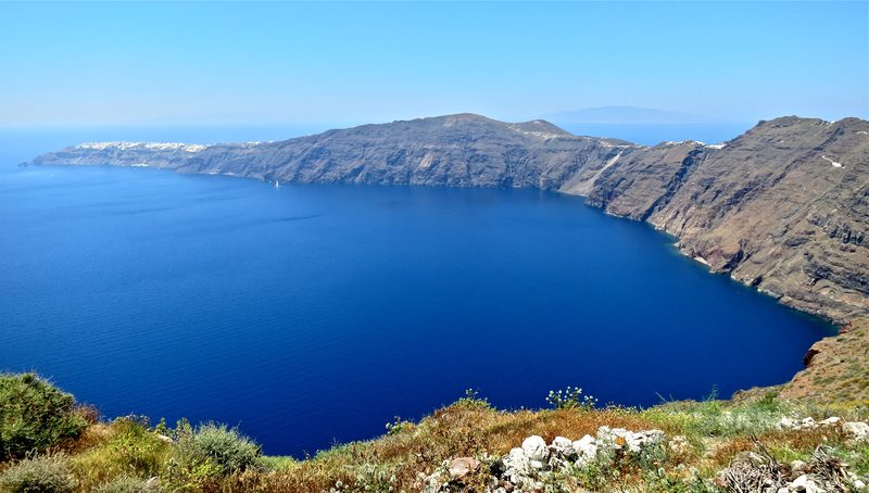 A scenic view of hikers on the ridge of the caldera in Santorini, with Oia town in the distance.