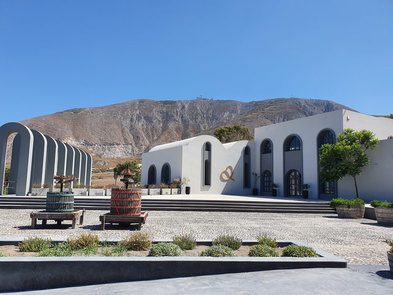 A Santorini winery courtyard with old wooden grape presses on display in front of the arched, whitewashed tasting rooms