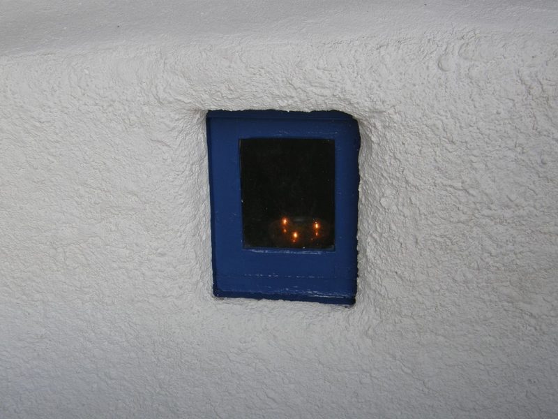 A window and lit candles in the small church of the Seven Kids at Finikia of Oia, Santorini.